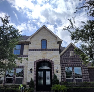 A beige stone and red brick two story home sparkling and spotless after receiving window cleaning 