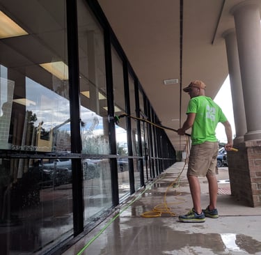 Technician in Clearly Organic Green uniform cleaning storefront windows with a water-fed pole