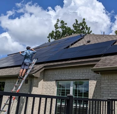 Technician cleaning solar panels on a residential roof with a squeegee pole