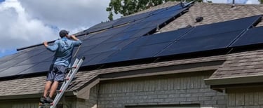 A man standing from a ladder cleaning solar panels on a roof with a water pool 