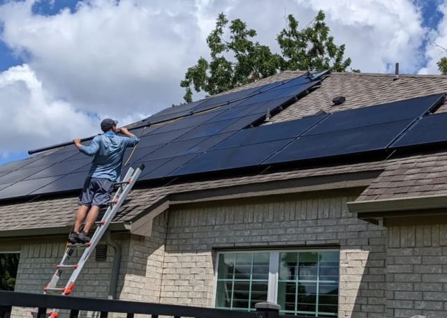 A man standing from a ladder cleaning solar panels on a roof with a water pool 